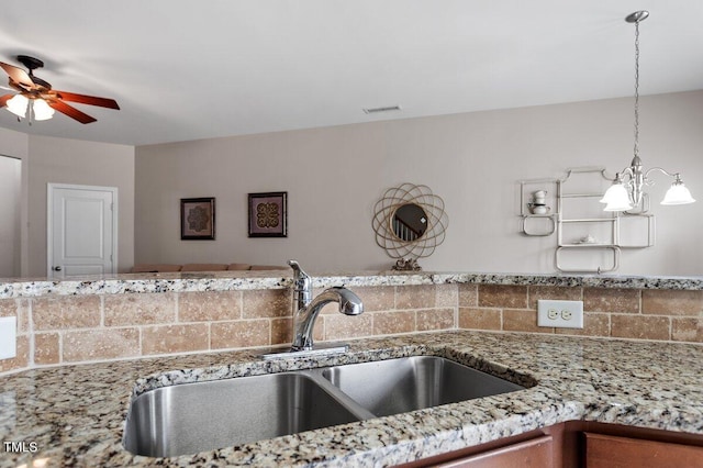 kitchen featuring a sink, a ceiling fan, light stone counters, and tasteful backsplash