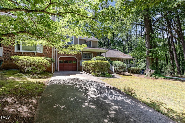 view of front facade featuring asphalt driveway, an attached garage, brick siding, a front yard, and covered porch