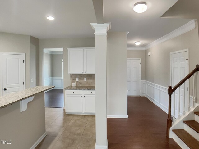 kitchen featuring light stone counters, white cabinets, a decorative wall, ornamental molding, and wainscoting