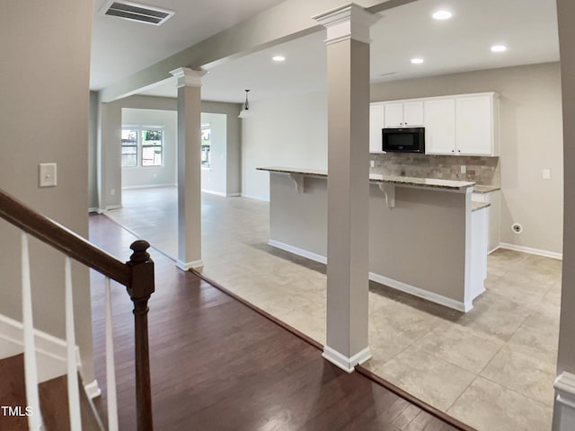 kitchen featuring black microwave, decorative columns, white cabinetry, a breakfast bar area, and decorative backsplash