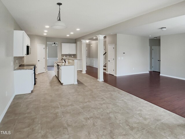 kitchen with a sink, ornate columns, open floor plan, a center island with sink, and white cabinets