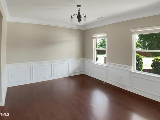 unfurnished room featuring a chandelier, healthy amount of natural light, ornamental molding, a wainscoted wall, and dark wood finished floors