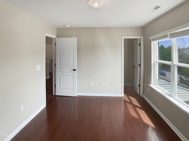 unfurnished bedroom with hardwood / wood-style flooring, baseboards, a walk in closet, and a closet