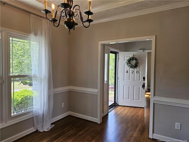 foyer entrance with crown molding, a chandelier, dark wood-type flooring, baseboards, and a textured ceiling
