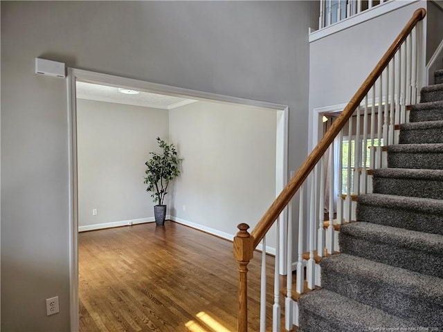 stairs with wood finished floors, baseboards, and crown molding