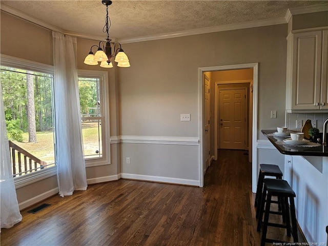 dining space featuring dark wood finished floors, a chandelier, a textured ceiling, crown molding, and baseboards
