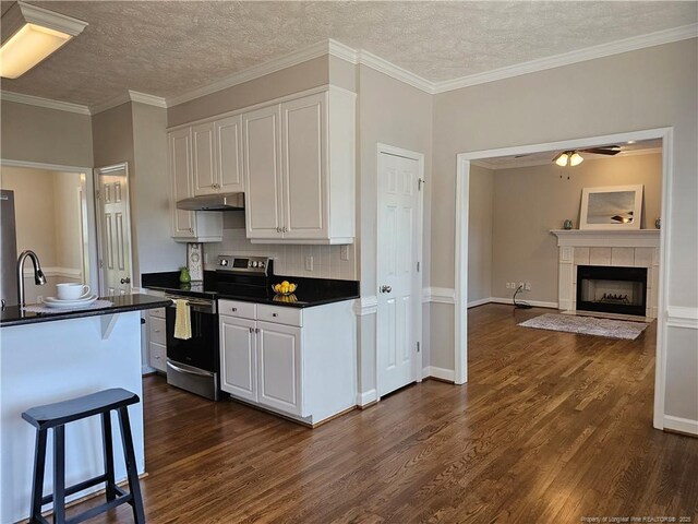 kitchen featuring stainless steel range with electric cooktop, under cabinet range hood, dark countertops, dark wood-style floors, and a textured ceiling