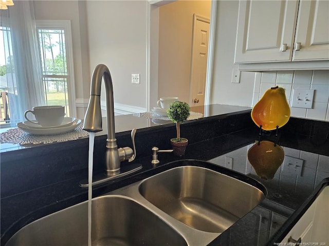 kitchen view of a sink, decorative backsplash, white cabinetry, and dark stone countertops