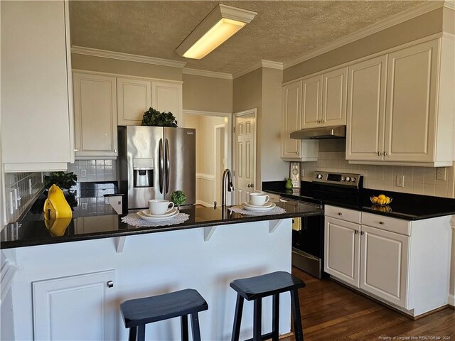 kitchen featuring stainless steel appliances, under cabinet range hood, a peninsula, dark countertops, and white cabinetry