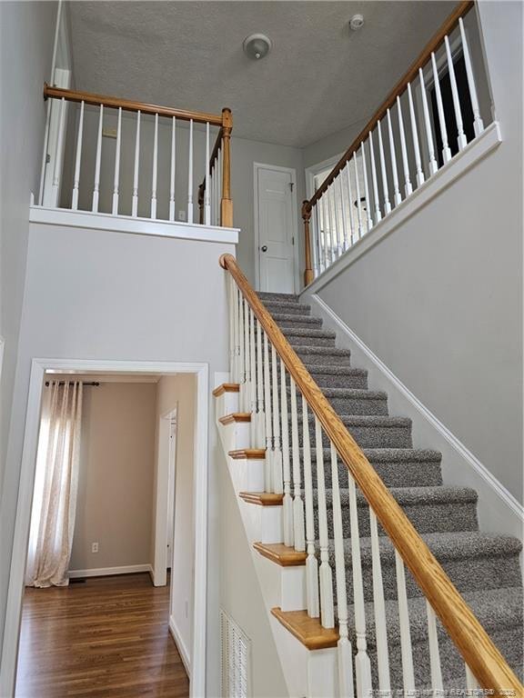staircase featuring wood finished floors, baseboards, and a high ceiling