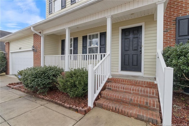 entrance to property with a porch, driveway, brick siding, and an attached garage