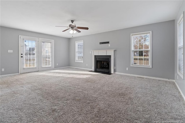 unfurnished living room featuring ceiling fan, a fireplace with flush hearth, baseboards, and carpet