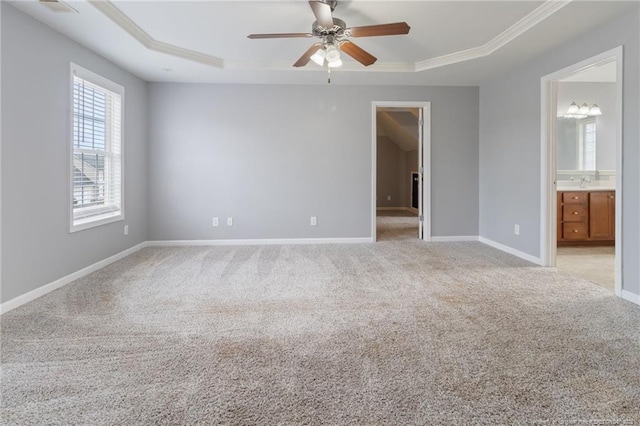 unfurnished bedroom with a raised ceiling, light carpet, crown molding, baseboards, and ensuite bath