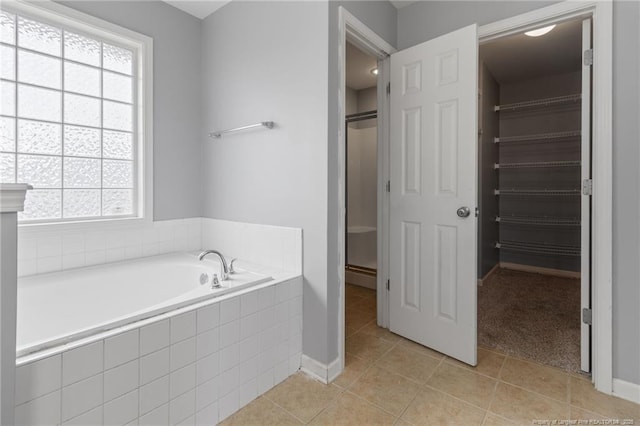 bathroom featuring tile patterned flooring, a stall shower, a spacious closet, a bath, and baseboards