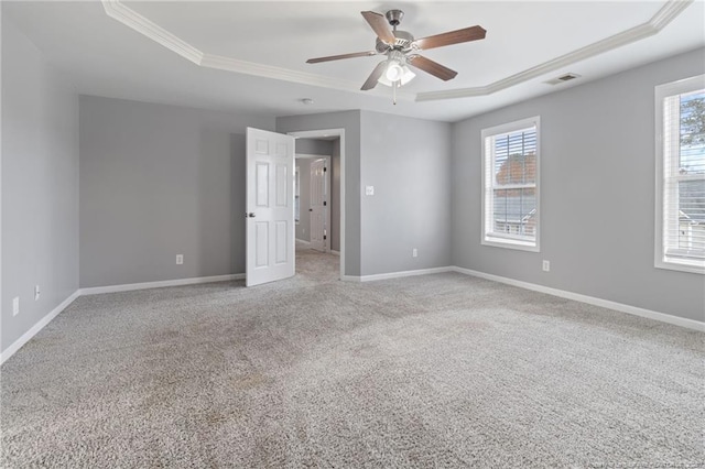 unfurnished bedroom featuring a raised ceiling, crown molding, multiple windows, and carpet floors