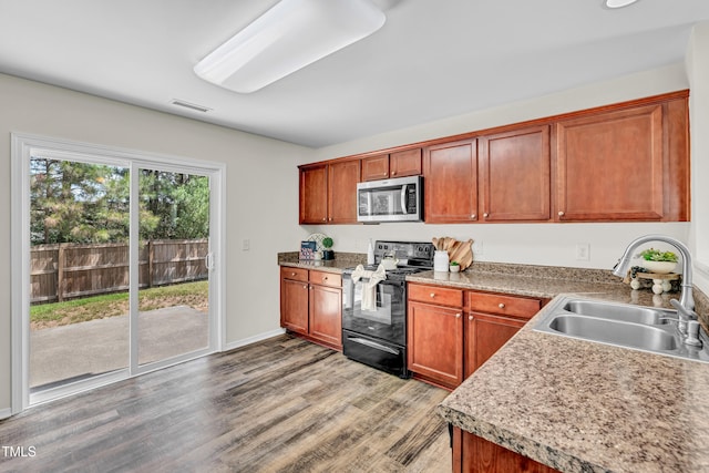 kitchen with black electric range oven, stainless steel microwave, a sink, light wood-type flooring, and light countertops