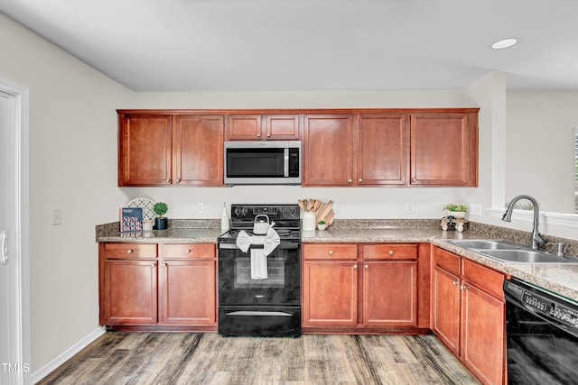 kitchen featuring black appliances, a sink, light wood-style floors, recessed lighting, and light stone countertops