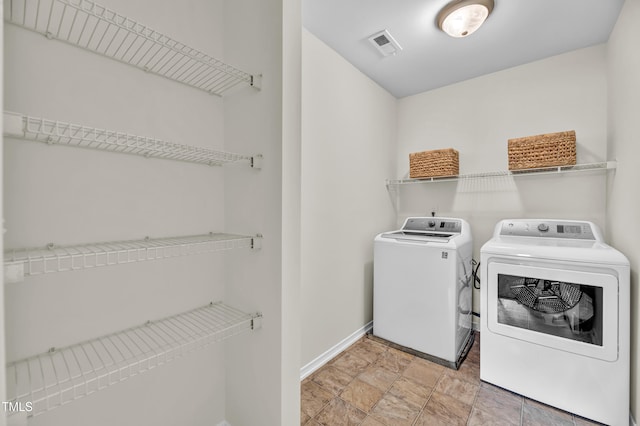 clothes washing area with baseboards, washing machine and dryer, and stone finish flooring