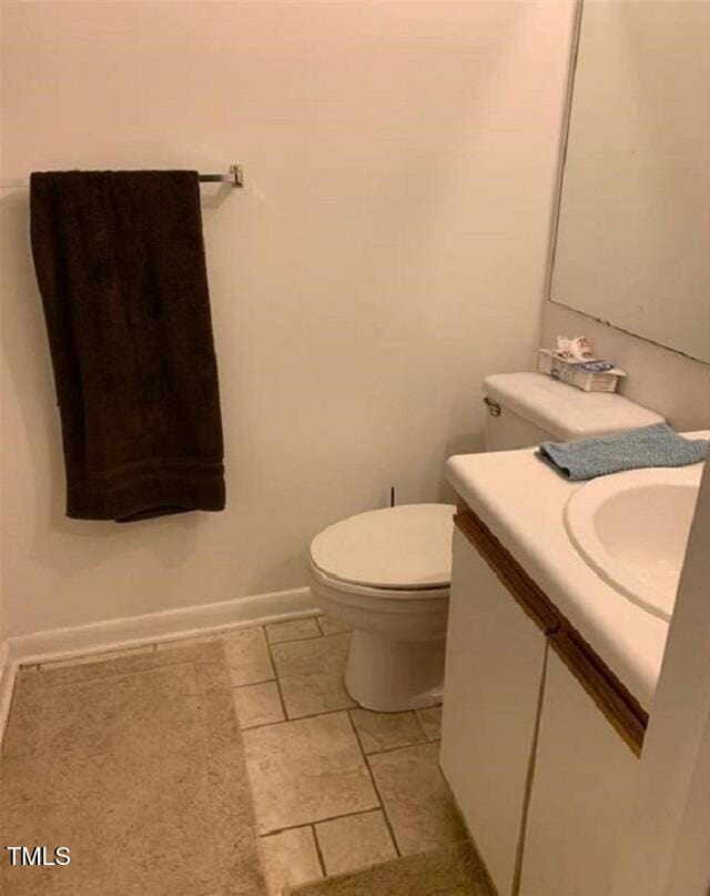 half bath with toilet, vanity, tile patterned flooring, and baseboards