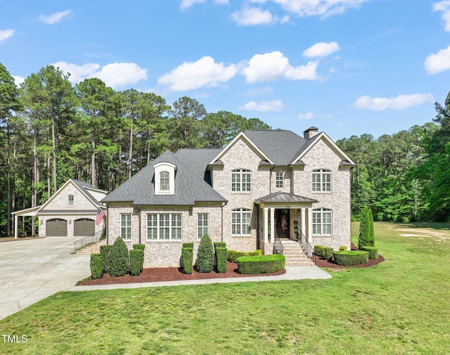 french country home featuring a chimney, a front yard, stone siding, an outdoor structure, and concrete driveway