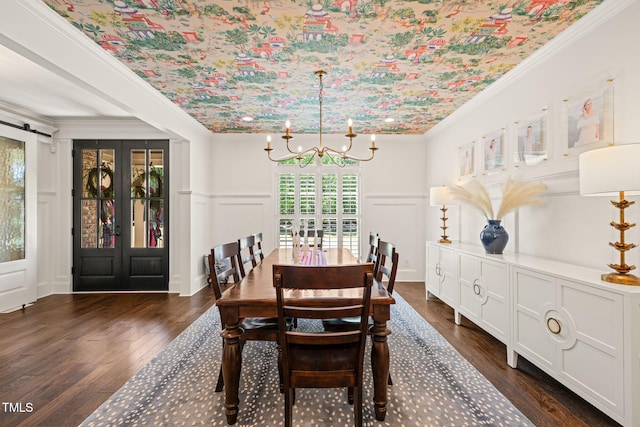 dining space featuring a decorative wall, a chandelier, dark wood-type flooring, crown molding, and wainscoting