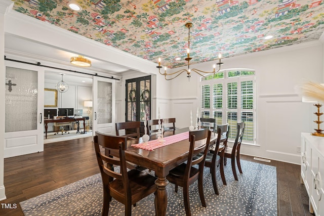 dining area with a decorative wall, a barn door, crown molding, dark wood-type flooring, and a chandelier