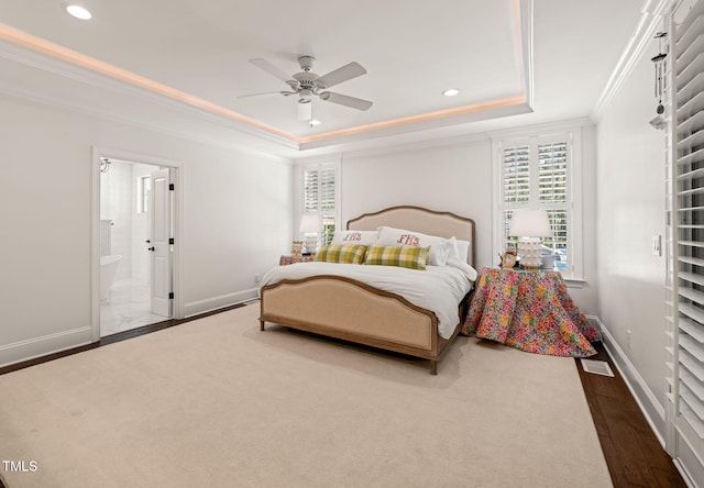 bedroom with baseboards, crown molding, a raised ceiling, recessed lighting, and ensuite bath