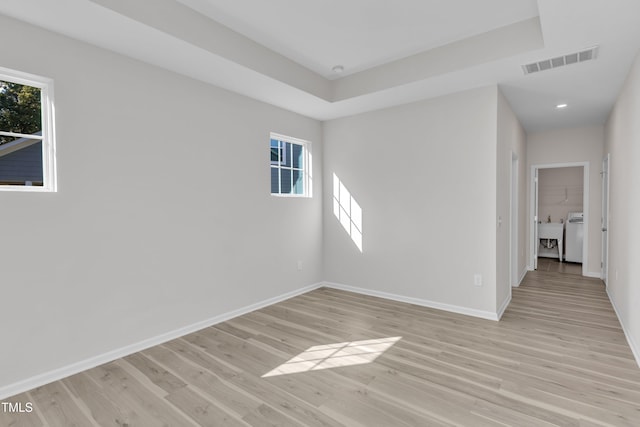 empty room with healthy amount of natural light, baseboards, light wood-type flooring, recessed lighting, and a raised ceiling