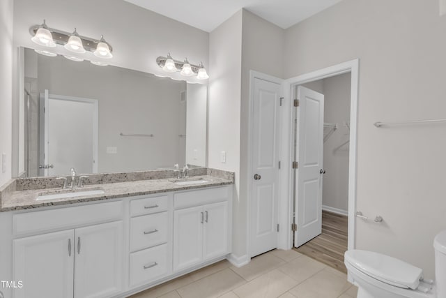 full bath featuring toilet, tile patterned flooring, double vanity, and a walk in closet