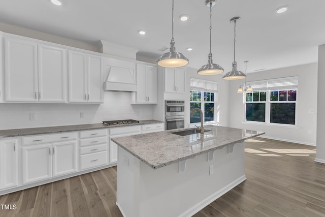 kitchen with a sink, recessed lighting, white cabinets, wood finished floors, and appliances with stainless steel finishes