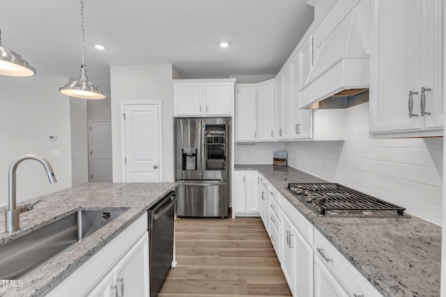 kitchen with stainless steel appliances, custom range hood, a sink, white cabinetry, and decorative backsplash