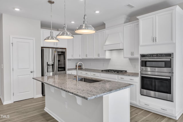 kitchen with a sink, light wood-style flooring, stainless steel appliances, white cabinetry, and light stone countertops