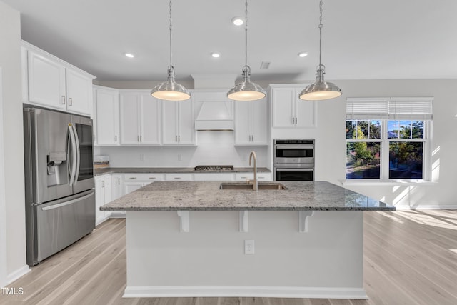 kitchen featuring appliances with stainless steel finishes, a sink, custom range hood, light wood-type flooring, and white cabinetry