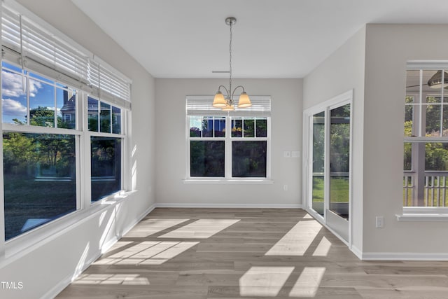 unfurnished dining area with a chandelier, wood finished floors, and baseboards