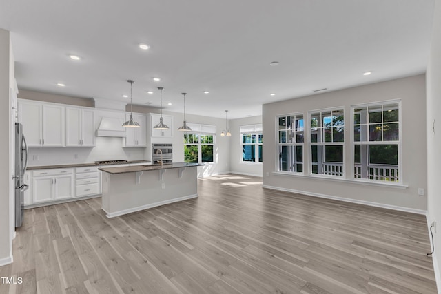kitchen featuring appliances with stainless steel finishes, premium range hood, dark countertops, a breakfast bar, and light wood-style flooring