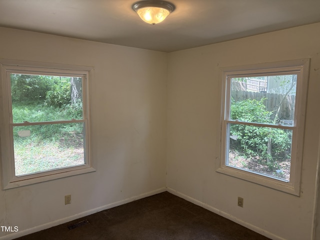 unfurnished room featuring plenty of natural light, baseboards, and dark carpet