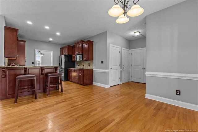 kitchen featuring freestanding refrigerator, light wood-style floors, a kitchen breakfast bar, a chandelier, and baseboards
