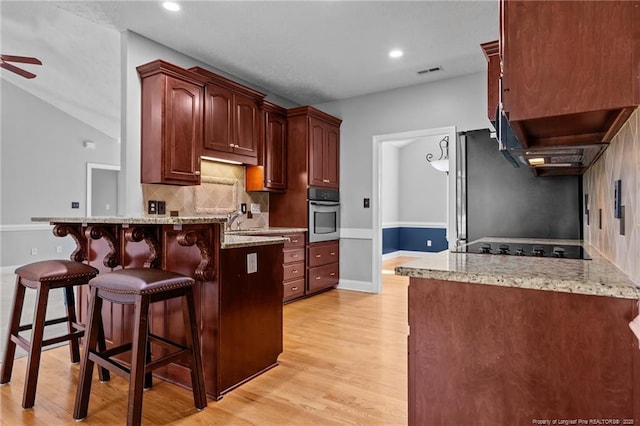 kitchen featuring stainless steel oven, a peninsula, a ceiling fan, a kitchen bar, and light wood-style flooring