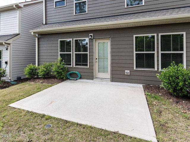 view of exterior entry with a patio area, a yard, and roof with shingles
