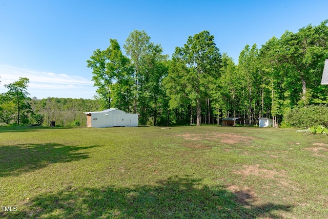 view of grassy yard featuring an outdoor structure, an outbuilding, and a view of trees