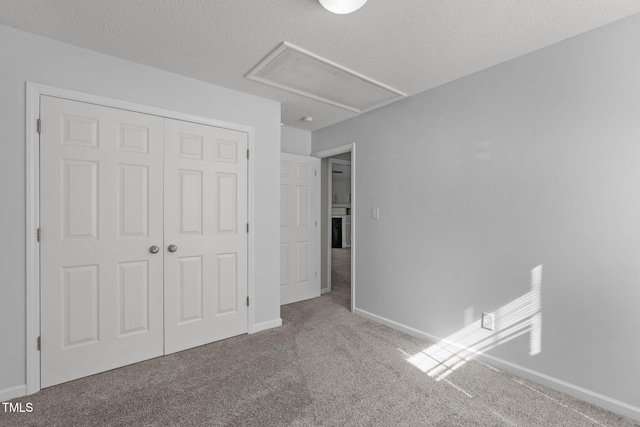 unfurnished bedroom featuring attic access, carpet, a closet, a textured ceiling, and baseboards