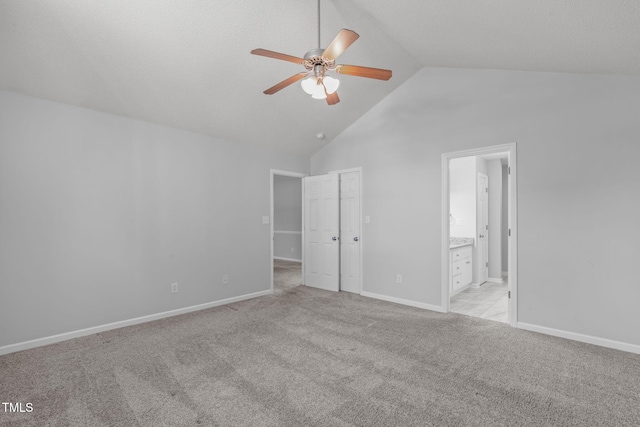 unfurnished bedroom featuring light colored carpet, ensuite bathroom, baseboards, high vaulted ceiling, and a ceiling fan