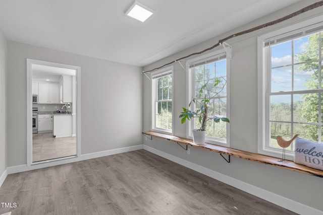 spare room featuring a sink, baseboards, and light wood-type flooring