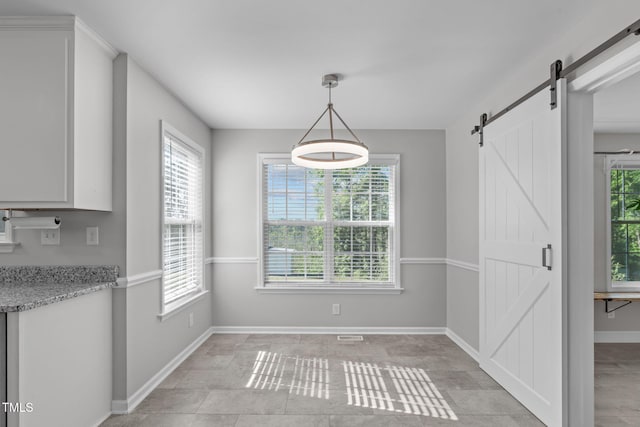 unfurnished dining area with a barn door, plenty of natural light, and baseboards