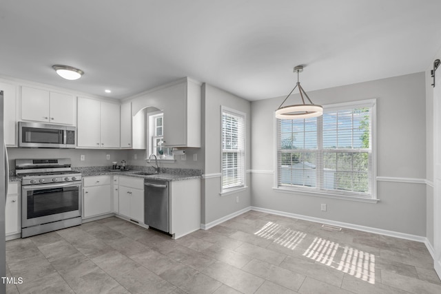 kitchen with appliances with stainless steel finishes, a sink, healthy amount of natural light, and white cabinetry