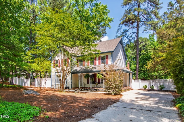 traditional-style house featuring covered porch, concrete driveway, roof with shingles, and fence