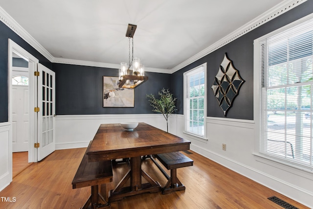 dining room featuring a chandelier, wood finished floors, a wainscoted wall, and ornamental molding