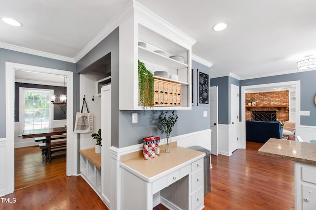 hallway featuring wood finished floors, ornamental molding, wainscoting, a chandelier, and a decorative wall