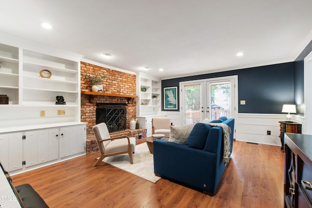 living room featuring light wood-type flooring, built in shelves, french doors, a wainscoted wall, and ornamental molding