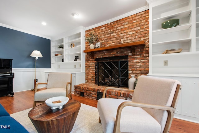 living area featuring ornamental molding, wainscoting, built in shelves, wood finished floors, and a fireplace